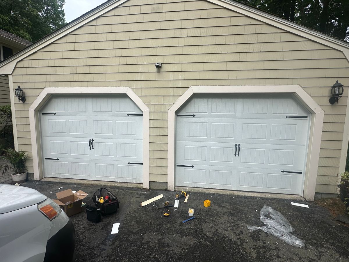White dual carriage-style doors with decorative hardware on shingle home